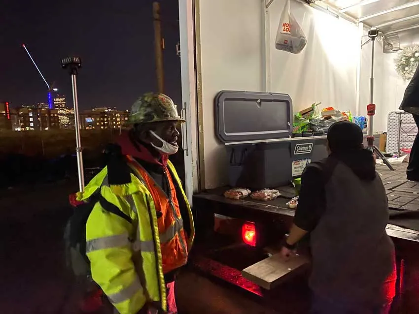 ARCM Roofing crew serving food from the ARCM truck at night with the Denver skyline behind